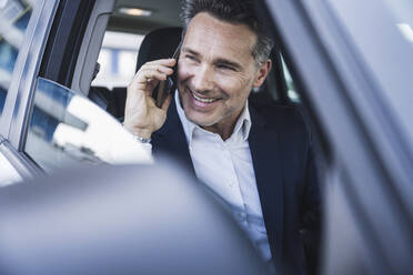 Glücklicher reifer Geschäftsmann, der im Auto mit seinem Smartphone telefoniert - UUF26389