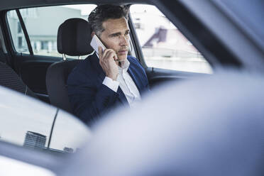 Älterer Geschäftsmann, der auf dem Fahrersitz im Auto sitzt und mit seinem Handy spricht - UUF26392