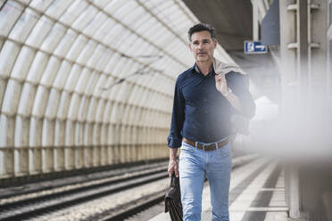 Älterer Geschäftsmann mit Tasche und Jacke auf dem Bahnhof - UUF26405