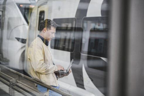 Geschäftsmann mit Tablet-PC vor einem Zug im Bahnhof stehend - UUF26427