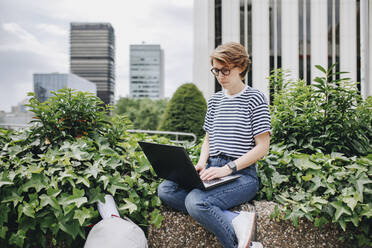 Geschäftsfrau mit Laptop inmitten von Pflanzen sitzend - MRRF02217