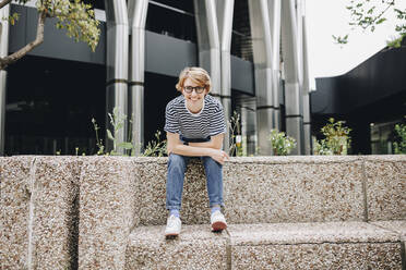 Smiling woman sitting on bench in front of office building - MRRF02229