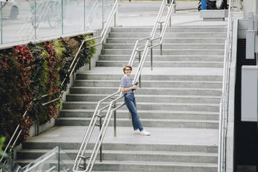 Glückliche Frau lehnt sich an das Geländer einer Treppe - MRRF02238
