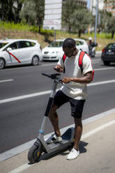 Junger Mann mit Elektroroller und Smartphone auf der Straße - OCMF02426