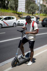 Young man with electric push scooter using smart phone on road - OCMF02426