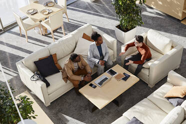 Junge Geschäftsleute und Geschäftsfrau diskutieren auf dem Sofa sitzend in einem modernen Büro die Strategie - DSHF00459