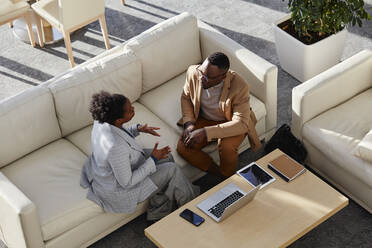 Geschäftsfrau tauscht Ideen mit einem Kollegen aus, der auf einem Sofa in einem modernen Büro sitzt - DSHF00461