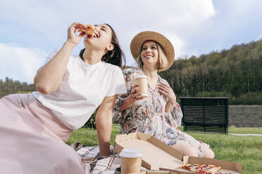 Woman eating pizza by friend in park on weekend - OMIF00881