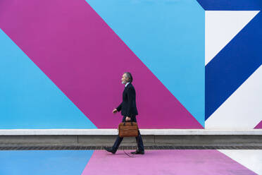 Businessman with bag walking in front of multi colored wall - OIPF02001