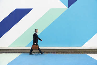 Älterer Geschäftsmann mit Tasche, der vor einer mehrfarbigen Wand geht - OIPF02002