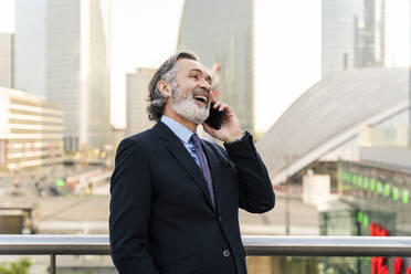 Fröhlicher Geschäftsmann mit grauem Haar, der mit einem Smartphone spricht - OIPF02035