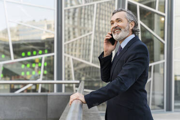 Happy businessman talking on smart phone standing by railing - OIPF02041