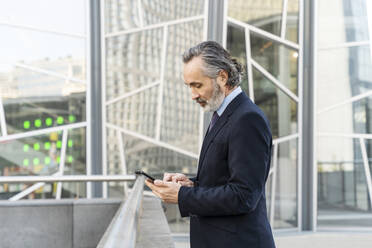 Mature businessman using mobile phone standing by railing - OIPF02042