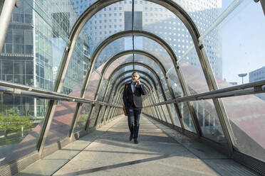 Älterer Geschäftsmann, der mit seinem Mobiltelefon spricht und auf einer Fußgängerbrücke geht - OIPF02044