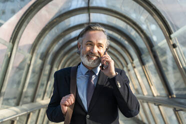 Happy mature businessman talking through smart phone on footbridge - OIPF02046