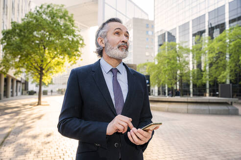 Älterer Geschäftsmann mit Mobiltelefon in einem Büropark - OIPF02055