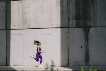 Junge Frau läuft auf dem Fußweg an der Mauer - OCMF02439