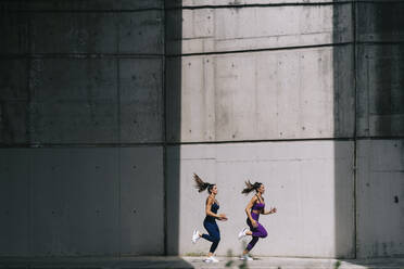 Twin sisters running on footpath by wall - OCMF02440