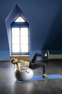Woman exercising with fitness ball in exercise room - RNF01361