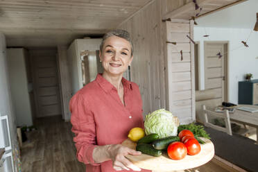 Lächelnde Frau hält Holzteller mit Gemüse - LLUF00555