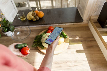 Woman holding smartphone with mobile app and vegetables - LLUF00556