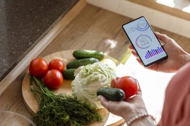 Woman holding smartphone with mobile app and vegetables - LLUF00557