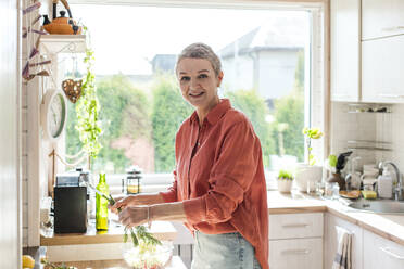 Smiling woman holding herbs in kitchen at home - LLUF00567