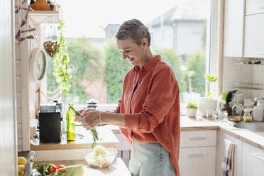 Frau hält Kräuter für Salat in der Küche zu Hause - LLUF00568