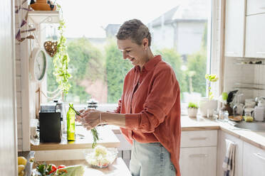 Woman holding herbs for salad in kitchen at home - LLUF00568