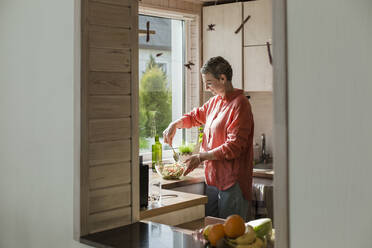 Frau am Fenster in der Küche bei der Zubereitung von Salat - LLUF00572