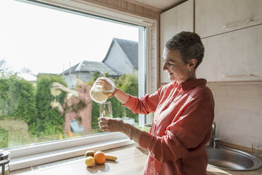 Frau in Küche gießt Fruchtsmoothie in ein Glas - LLUF00575