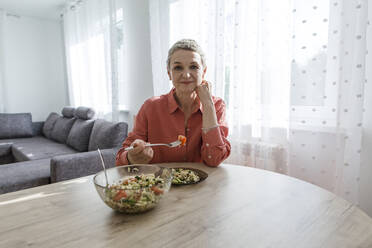 Frau isst Salat am Holztisch zu Hause - LLUF00576