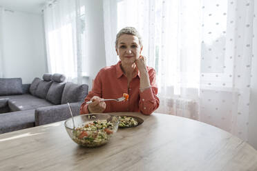 Woman eating salad at wooden table at home - LLUF00576