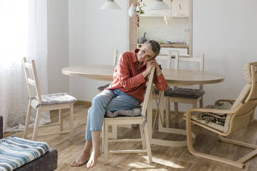 Relaxed woman sitting on chair at wooden table at home - LLUF00580