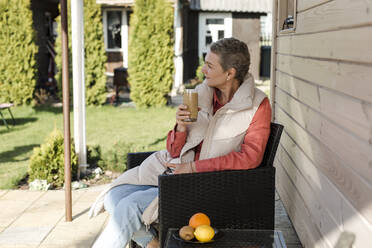 Frau sitzt auf Veranda und hält Smoothie - LLUF00586