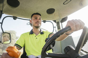 Young farmer driving tractor on sunny day - JCMF02275