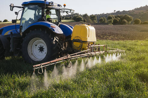 Landwirt beim Sprühen von Dünger durch eine im Traktor sitzende Spritze auf einem Feld - JCMF02287