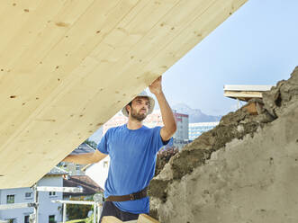 Young man working at construction site on rooftop of house - CVF01966