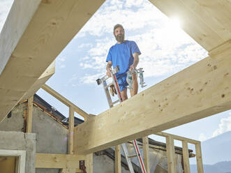 Junger Mann steht auf einer Leiter auf einer Baustelle - CVF01967