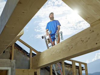 Junger Mann steht auf einer Leiter auf einer Baustelle an einem sonnigen Tag - CVF01968