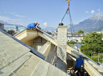 Arbeiter bei der Montage von Holzbrettern auf dem Dach mit einer Kranmaschine - CVF01973