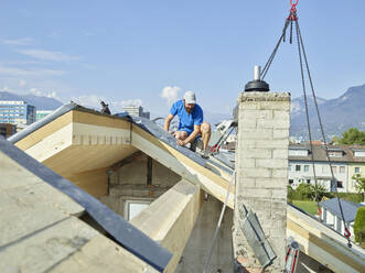 Junger Mann bei der Montage von Holzbrettern auf dem Dach mit einem Kran - CVF01974