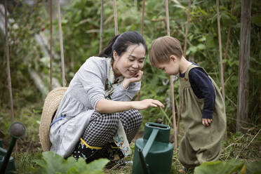 Mother and toddler son with watering can in garden - CAIF32775