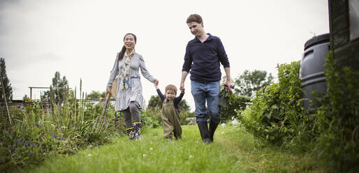 Family holding hands and walking in garden grass - CAIF32783