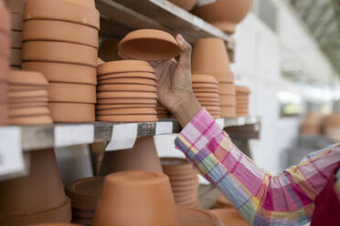 Hand of gardener stacking clay saucers on shelf in warehouse - JCCMF06408