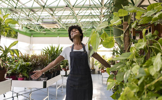 Carefree gardener with arms outstretched enjoying by plants at nursery - JCCMF06471