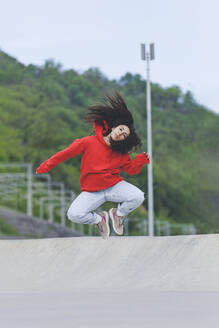 Frau mit zerzaustem Haar springt im Skateboardpark - OMIF00887