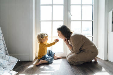 Glücklicher Sohn spielt mit seiner Mutter, die zu Hause am Fenster sitzt - VPIF06259