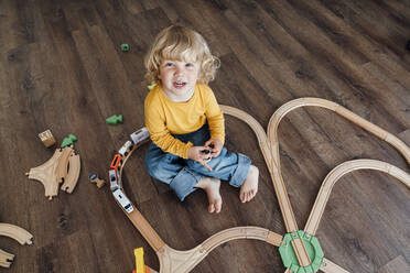Glücklicher Junge mit blondem Haar, der mit einer Spielzeugeisenbahn zu Hause spielt - VPIF06263