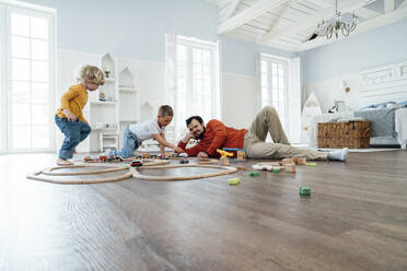 Brothers playing with toy train set by father lying at home - VPIF06265